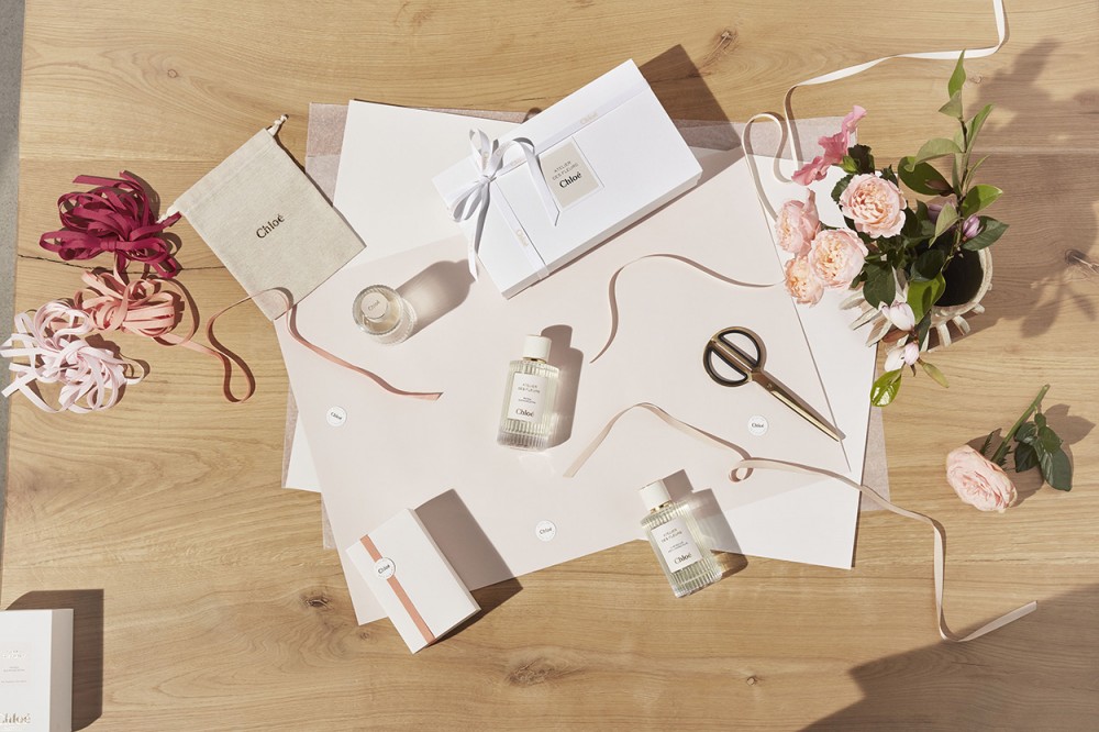 百摺紋玻璃瓶頂部是象牙白瓶塞,瓶身的絲帶和米色標籤的鑲邊飾滿金色