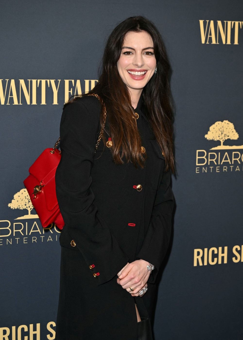 身穿Versace 2024 秋冬系列的羊毛華達呢長制服外套,飾有美杜莎紐釦和口紅色釦眼,搭配皮革迷你裙和 Versace Texano 靴子搭配紅色Kleio單肩包完成整體造型。