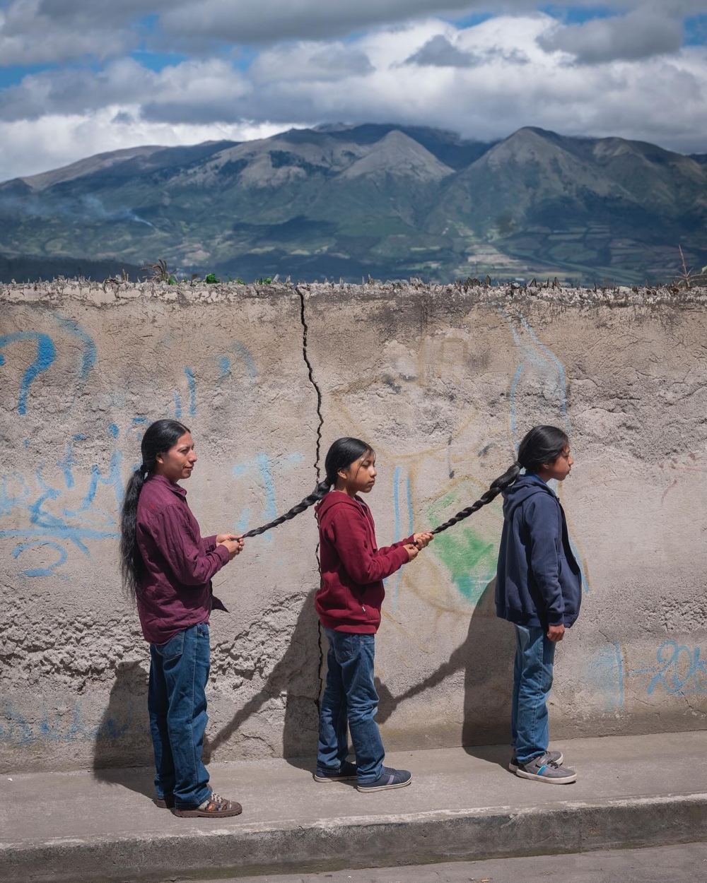 一位父與他的兩個兒子站在水泥牆前,幫對方編編辮子