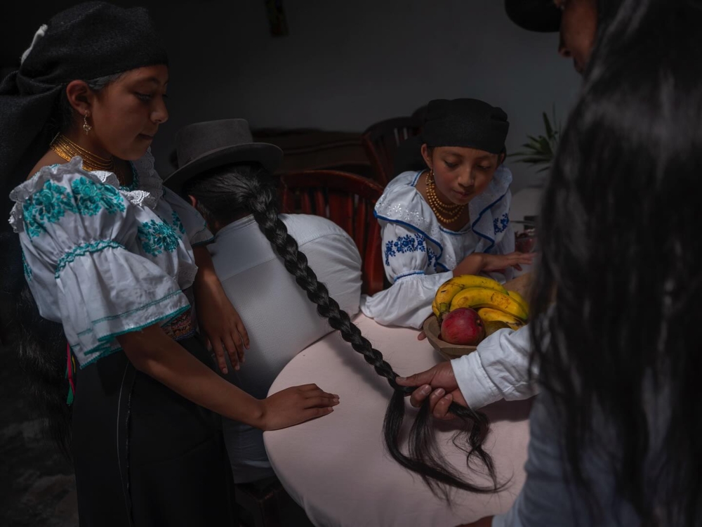 在厄瓜多爾奧塔瓦洛基丘亞社區,男子正在為兒子編辮子,女兒們則在一旁觀看