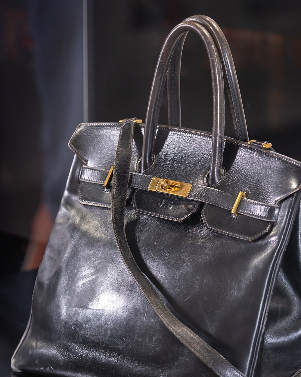 包身布滿了歲月痕跡:黑色皮革表面磨損發亮,翻蓋、提把和邊角處都有明顯的使用痕跡。